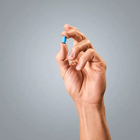 A hand holding a small blue pill representing the healthcare industry