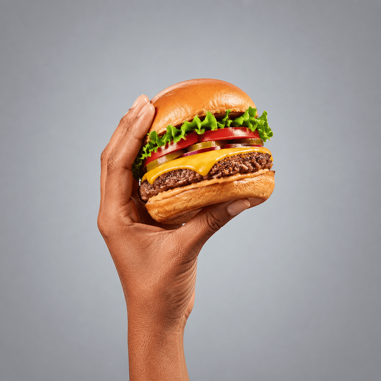 A hand holding a cheeseburger representing the quick-service hospitality industry