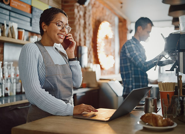 A coffee shop owner reviewing financial reports on her laptop using American PaySave's merchant portal