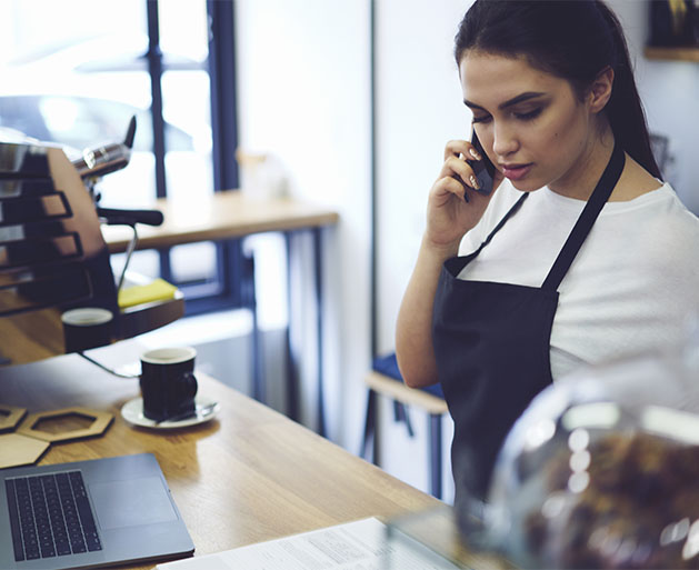 A coffee shop employee on her phone, looking at customer management tools provided by American PaySave's POS systems