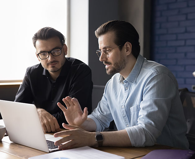 Two men at laptops discussing American PaySave's intergraded payment processing systems